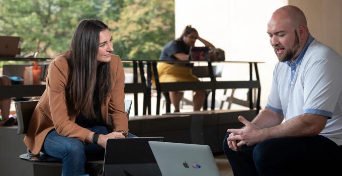 two people sit on the posvar patio with laptops in front of them. they are in conversation.