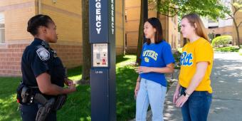 a pitt police office speaks to two students on campus