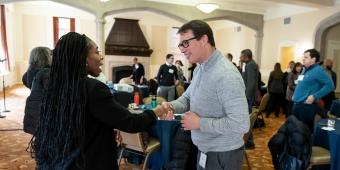 a man shakes a woman's hand. they are greeting one another and in conversation