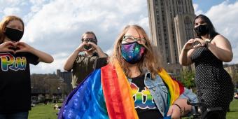 students pose for a photo wearing pride gear and draped in a pride flag